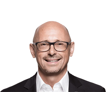 Günther Rossdeutscher, geschäftsführender Gesellschafter bei asecos, blickt freundlich in die Kamera. Er trägt eine dunkle Brille, ein weißes Hemd und ein dunkles Sakko. Er ist glatzköpfig mit kurzem Bart.