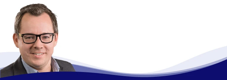 Dominik Fimberger, Head of Marketing and E-Commerce at Weyland Steiner, smiles at the camera. He is wearing dark-rimmed glasses, a light blue shirt with an open collar and a gray jacket over it. His hair is short and brown and he has no beard.