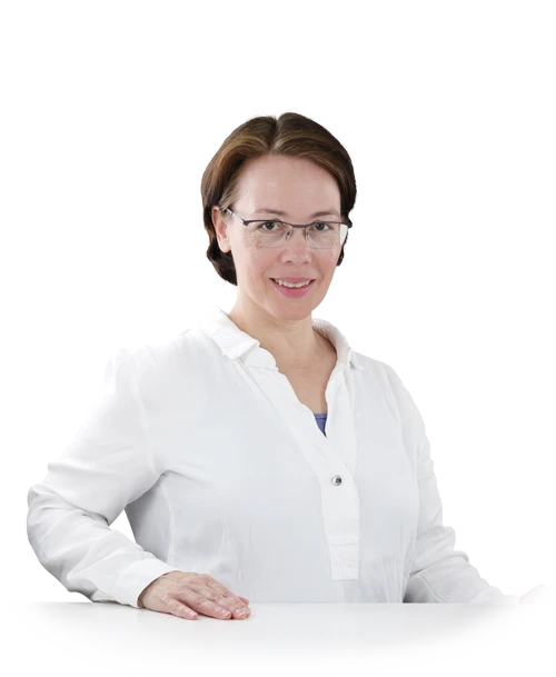 Rosa Sanchez is standing at a table in a white blouse tunic. She has placed her hands on the tabletop and is smiling at the camera.